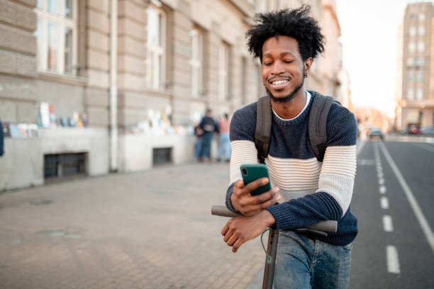 istock Young man using phone while riding an electric push scooter around the city 1220861396