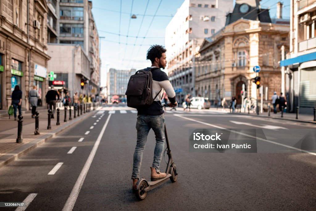 Young man with curly hairstyle riding an electric push scooter around the city - Royalty-free Trotinete Foto de stock