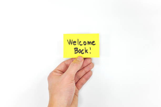 Hand holding a welcome back note on yellow card. Back to work, office, business and school. White background.