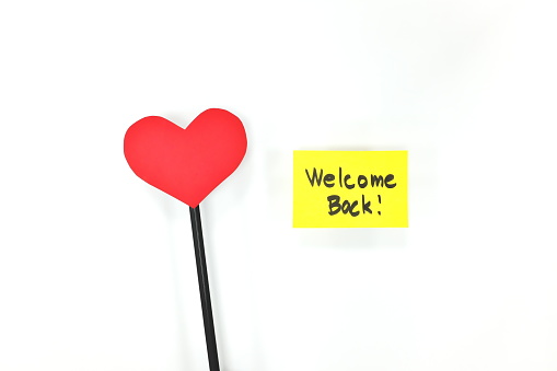 Welcome back note on yellow card with a red heart. Back to work, office, business and school. White background.