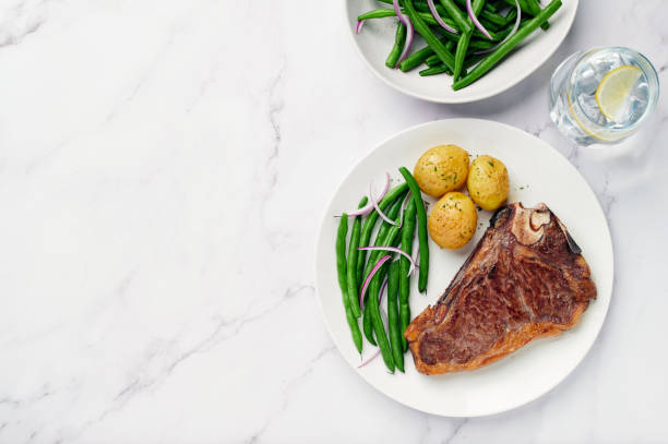 Dry Aged Beef Steak with potatoes and green beans Dry Aged Beef Steak with potatoes and green beans.Dry aged  sirloin steak with green beans salad and glass of water on white marble table with copy space green bean vegetable bean green stock pictures, royalty-free photos & images