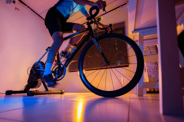 homem asiático pedalando no treinador de máquinas que ele está exercitando em casa à noite.ele joga jogo de bicicleta online - short cycle - fotografias e filmes do acervo