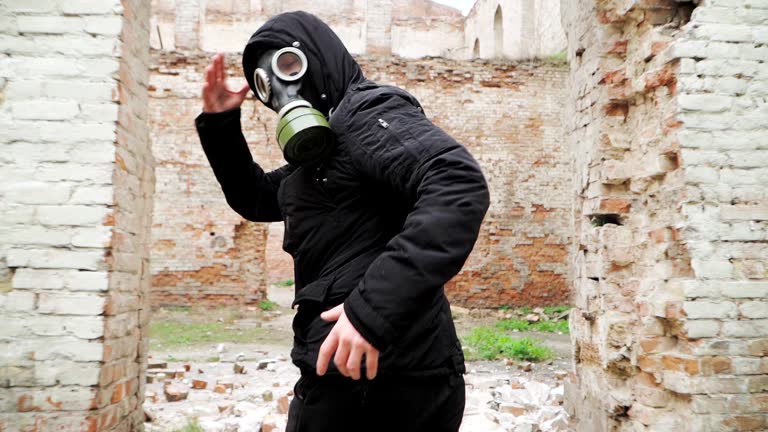 Man in gas mask and black clothes runs on an abandoned ruined building. Stalker concept, survivor after nuclear chemical war. Slow motion.