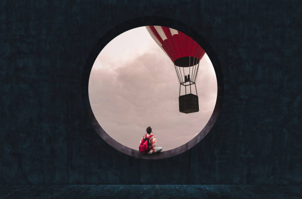 Man with a backpack looking through a round concrete window to a hot air balloon flying.