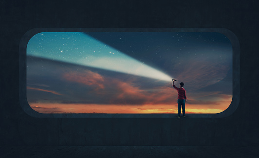 Young man light up the sky with a flashlight during dramatic sunset .