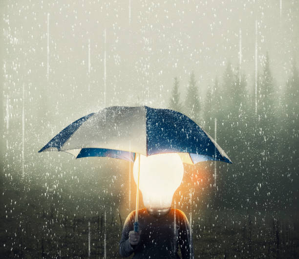 istock Man with a lightbulb instead of head holding umbrella while raining .  Positive mindset concept. 1220889470