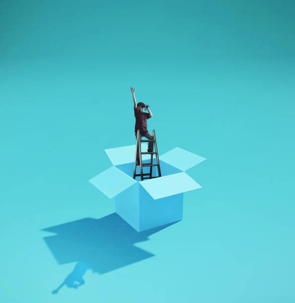 istock Man on a ladder looking through binoculars . Think outside the box concept . 1220889996