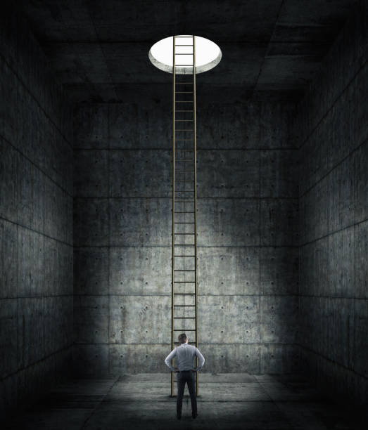 Businessman in a dark concrete room with a ladder to the  hole . Finding solution in tough times . Way out of problems, career opportunity. Businessman in a dark concrete room with a ladder to the  hole . Finding solution in tough times . Way out of problems, career opportunity. prison lockdown stock pictures, royalty-free photos & images