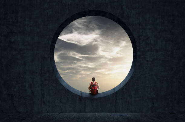 istock Man with a backpack looking through a round concrete window to sunset sky. 1220890082
