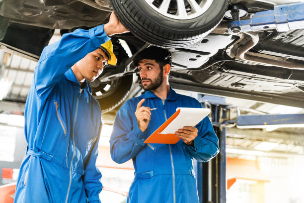 istock Mechanic in blue work wear uniform inspects the car bottom with his assistant. Automobile repairing service, Professional occupation teamwork. Vehicle maintenance. 1220894830