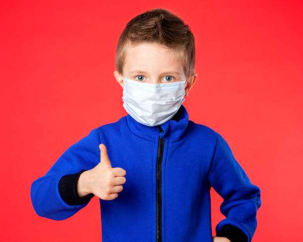 istock A boy in a medical mask shows super class on a red background. 1220895453