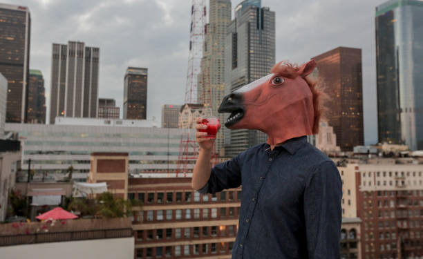 l'uomo che indossa la maschera della testa di cavallo si rilassa sul tetto con da bere - horse men animal head bizarre foto e immagini stock
