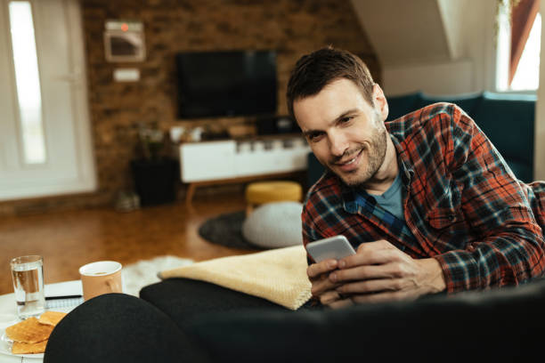 istock Happy man typing text message on cell phone while relaxing in the living room 1220907255