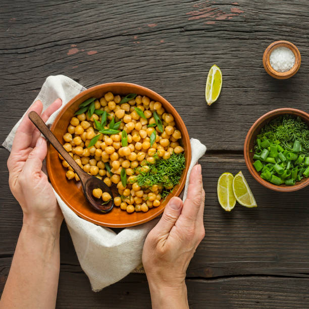 Healthy food. Chickpeas garnish. Woman serves boiled chickpeas in a bowl on a dining table. Vegetarian food