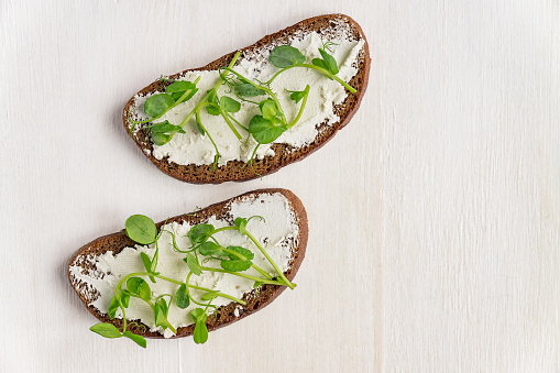Sandwiches on rye toast with fresh peas microgreen and cream cheese on white background. Top view. Copy space.