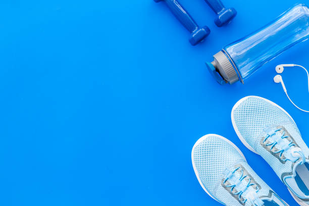 istock Fitness accessories. Dumbbells and sneakers on blue table top view copy space 1220913288