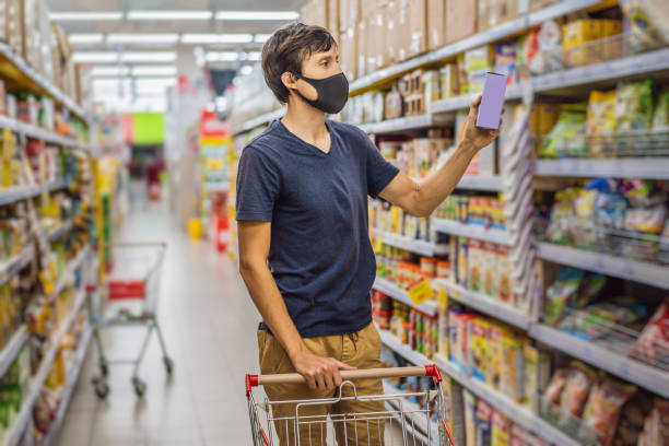 Alarmed man wears medical mask against coronavirus while grocery shopping in supermarket or store- health, safety and pandemic concept - young woman wearing protective mask and stockpiling food Alarmed man wears medical mask against coronavirus while grocery shopping in supermarket or store- health, safety and pandemic concept - young woman wearing protective mask and stockpiling food. bazaar market photos stock pictures, royalty-free photos & images