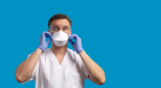 A male doctor in white uniformput puts on the protective surgical mask stock photo