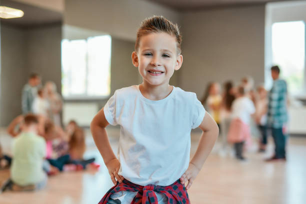 Cool dancer. Portrait of a cute and happy little boy in white t-shirt keeping arms on hips and looking at camera with smile while standing in the dance studio Cool dancer. Portrait of a cute and happy little boy in white t-shirt keeping arms on hips and looking at camera with smile while standing in the dance studio. Choreography class. Dance school dancing school stock pictures, royalty-free photos & images