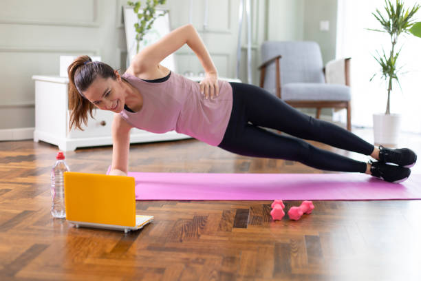 Beautiful sporty cheerful woman is doing side plank exercise Young woman exercising at home in a living room. Video lesson. She is repeating exercises while watching online workout session. bodyweight training stock pictures, royalty-free photos & images