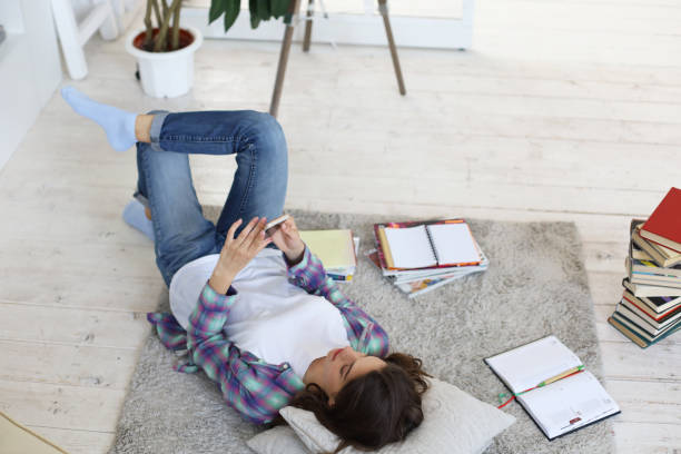 istock Distance learning. Young female student checking social media before getting back to studying, lying on floor. 1220942407