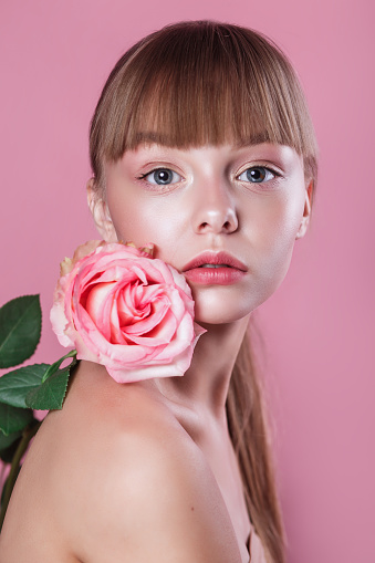 Beauty portrait of beautiful woman model with fresh daily makeup and rose on pink studio background