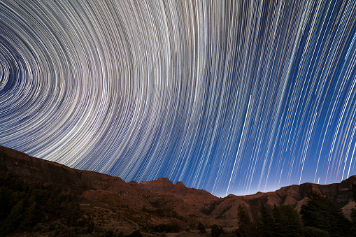 A magical circular star trail night sky photograph of the stars moving above the dramatic Drakensberg mountain range in South Africa.