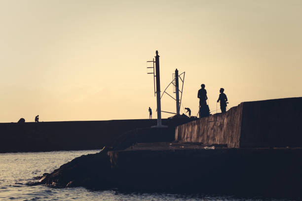 fishermen silhouettes at sunset in the harbor of saint gilles, la reunion island, mascarene islands, french overseas territory.