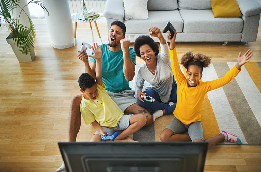 Closeup top view of a young african american family with two children spending time at home during coronavirus pandemic in 2020. They are playing some video games in the living room. 
For later use this is a quite useful family lifestyle content.