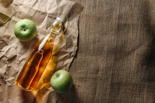 eine glasflasche mit apfelsaft und zwei grünen äpfeln liegen auf kraftpapier und sackleinen - burlap fruit apple freshness stock-fotos und bilder