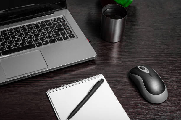 istock home office work desktop close-up.  Keyboard laptop mouse indoor flower white notebook and black pen on a wooden table. Telework office. Work remotely concept. 1220956190