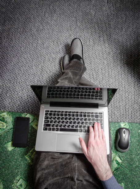 istock work home workplace concept top view. A man works at home on the sofa legs in slippers behind a laptop, calls on the phone, mouse. 1220959697