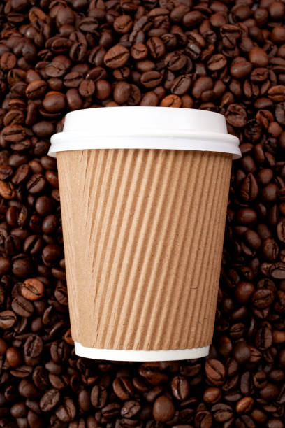 istock Arabica coffee aroma and takeout beverages concept with generic recyclable brown cardboard and paper cup with white plastic lid on full frame made of roasting coffee beans with vertical crop 1220964481