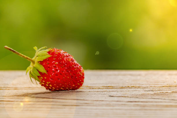 istock one strawberry on a wooden table with green bokeh 1220967934