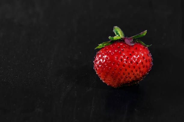 istock one strawberry on a black wooden background 1220967970