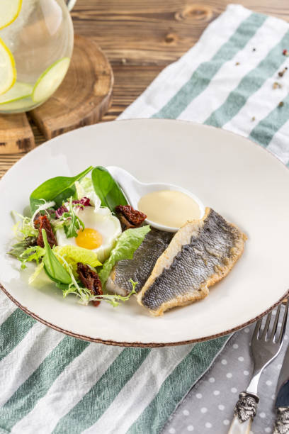 istock Fried white fish fillet with fried egg and greens on white plate on wooden table 1220969953