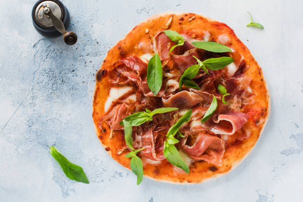 istock Homemade pizza with jamon, mozzarella and fresh basil leaves on a light concrete old background. Top view. 1220971127
