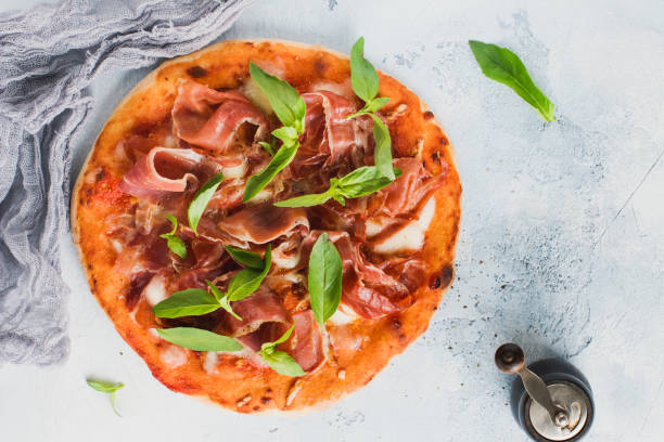 istock Homemade pizza with jamon, mozzarella and fresh basil leaves on a light concrete old background. Top view. 1220971251