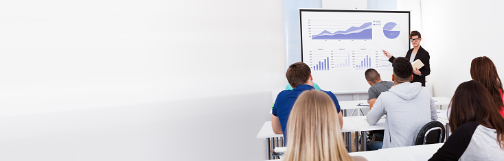 Young teacher teaching graphs drawn on whiteboard to college students in classroom