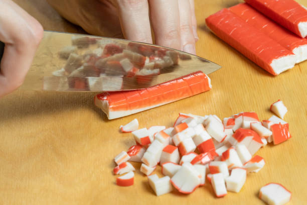 istock Women's hands cut crab sticks on a wooden board close up 1220974302