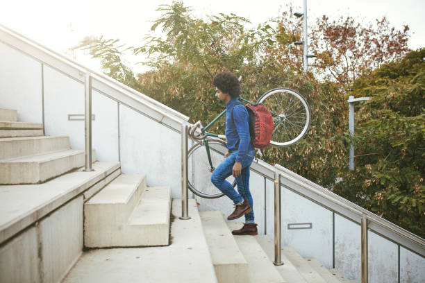 Mid Adult Commuter With Backpack Carrying Bicycle Up Stairs