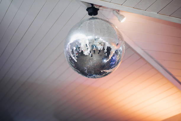 istock Spheric disco ball on the ceiling.Close-up of silver shining disco ball fixed on the white wooden ceiling at the party. 1220975963