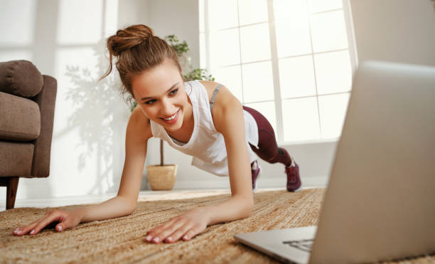 Young woman doing abdominal exercise in room with laptop