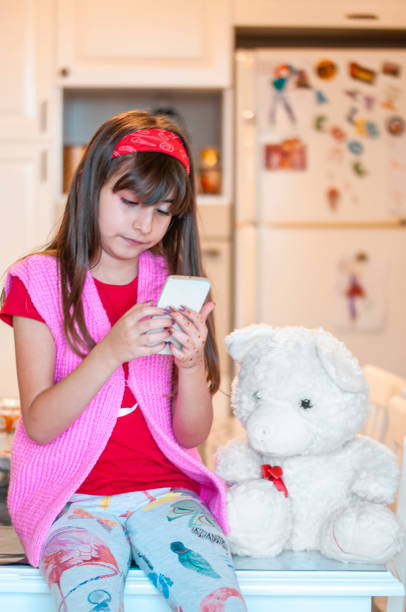 istock Littel girl using mobile phone at home with her teddy bear 1220983930