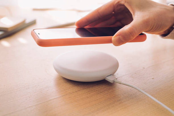 Hand of a Woman Placing her Smartphone onto a Wireless Charger, a Close Up Wireless charging: a mobile phone being placed on a modern wireless power bank. mobile phone charger stock pictures, royalty-free photos & images