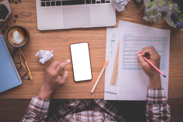 istock wood office table with businessman checking report paper, blank screen on mobile. 1220988794