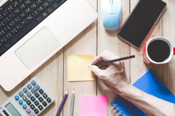 istock top view working desk. business man work on workspace use pencil writing a sticky note with copy space on wood table. 1220992114