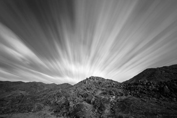 An arid black and white mountain landscape, using a long exposure to blur the fast moving clouds with fascinating geology and rock formations in the background, taken in the Richtersveld South Africa.