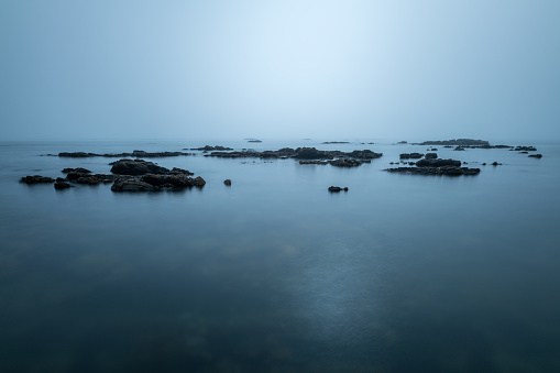 A long exposure seascape photographed on an overcast day in the small fishing village of Port Nolloth, South Africa, with the misty blue sea enveloping the rocks.