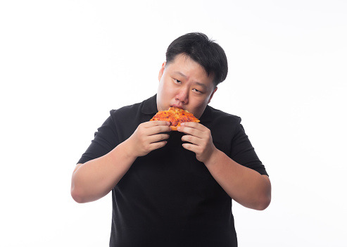 Happy young asian fat man in black polo shirt eating pizza isolated over white background.